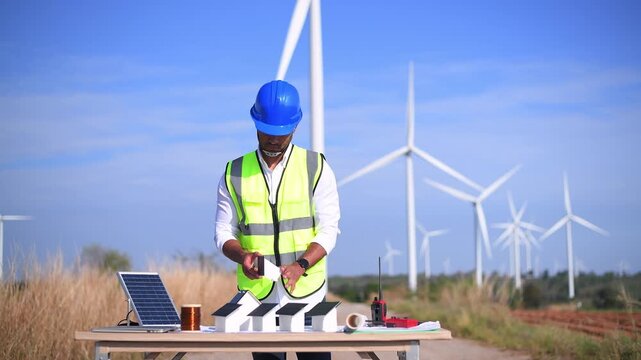 Engineer wearing uniform ,helmet inspection and survey work in wind turbine farms rotation to generate electricity energy. Green ecological power energy generation wind sustainable energy concept.	