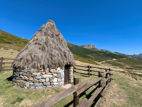 Traditional circular stone hut with conical thatched roof and wooden fence in a mountain pasture under a blue sky, Vegarada Pass, border of Asturias and Le&oacute;n, Spain