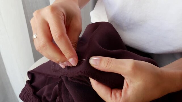 Close-up of woman sewing clothes by hand with needle and thread for clothing repair