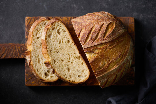 Sliced artisan sourdough bread, tartine loaf on wooden cutting board. Dark background. Close up. Top view.