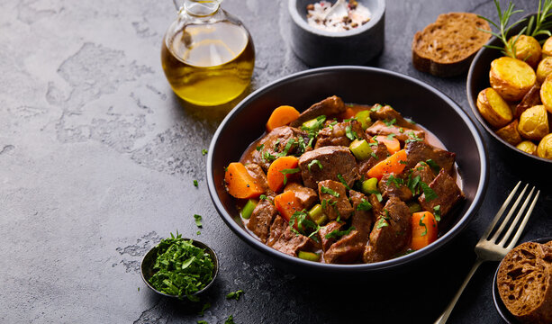 Traditional meat goulash served with roasted potatoes, bread and olive oil. Slate stone background. Copy space, close up.