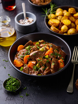 Traditional meat goulash served with roasted potatoes, bread and olive oil. Slate stone background.