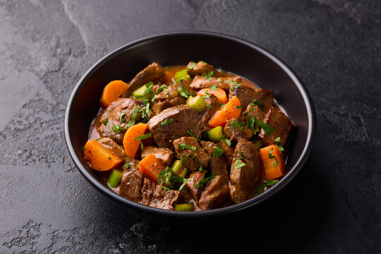 Beef stew with carrots and celery in a black bowl. Slate background. Close up.
