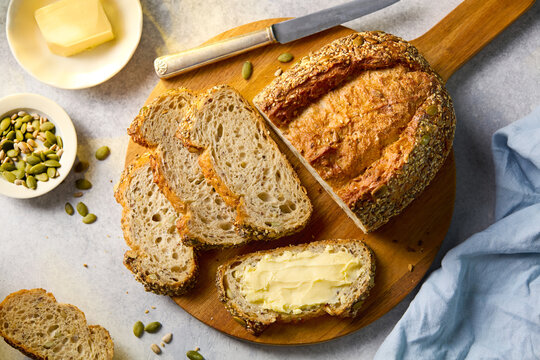 Sliced artisanal sourdough pumpkin seed loaf with dairy butter and a knife. Grey background. Close up. Top view.
