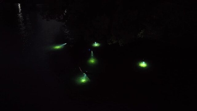 An aerial view shows snorkelers exploring a shallow underwater habitat at night in Lembeh Strait, Indonesia. This area of North Sulawesi is famous for its rare, black sand-associated marine life.