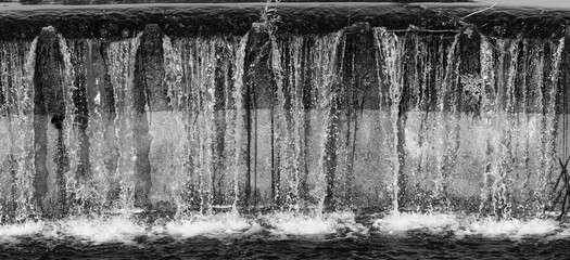 A high-contrast black-and-white close-up of a spillway (weir) where water cascades down in dense veils © Christian Bunge