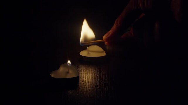 Close-up, hand with a burning match lighting candles standing on a table in a dark room