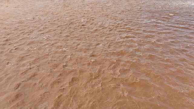 Drone view reveals powerful brown floodwater filled with sediment, reflecting intense rainfall, rain bomb conditions, climate change, extreme weather and rising disaster risks.
