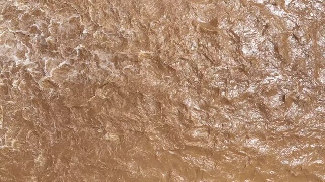 Aerial view captures turbulent muddy flash flood water surging with strong currents, illustrating global warming, extreme weather, rain bomb events, erosion and flood hazards. 4k.
