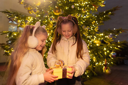 Girls exchange Christmas gift by illuminated festive tree