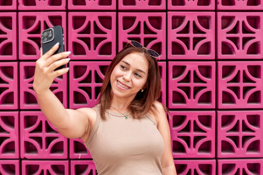 Smiling woman take smartphone selfie against pink wall