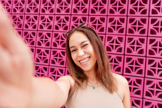 Smiling woman take selfie against pink patterned wall