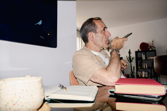 Senior man recording voice message on smartphone beside books at home