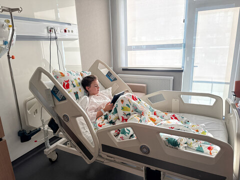 Child patient use tablet in bright hospital bed