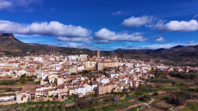 Panoramic view of Chelva, a traditional Spanish village in Valencia region, with white houses, church tower, surrounding mountains and blue sky with clouds