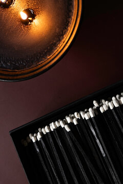 Long black matches in a box next to a burning candle