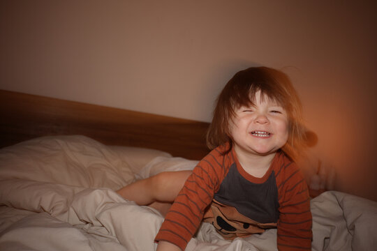 Child Smiles While Sitting on Bed in Bedroom at Night