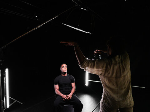 Photographer shooting male model in dark studio setting