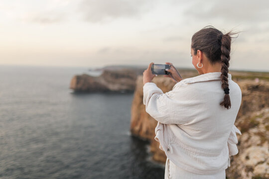 Woman photographing Cape Saint Vincent cliffs in Portugal