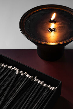 Long black matches in a box next to a burning black candle
