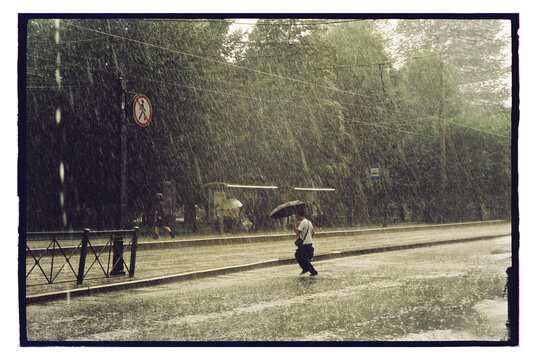 Heavy rain falls on a street as a man walks with an umbrella during