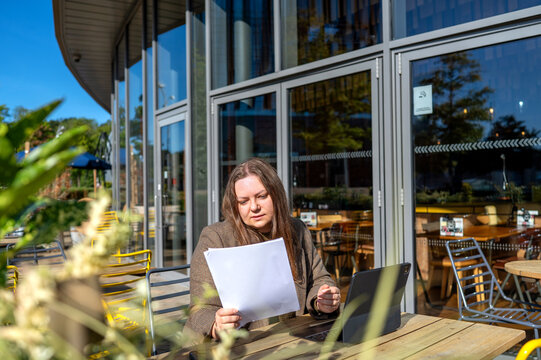 Freelancer review document at outdoor cafe with laptop