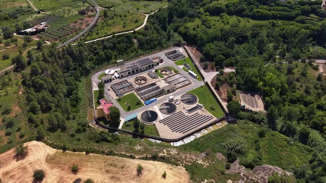 Top-down view of a municipal water treatment facility with circular clarifier tanks and rectangular basins, surrounded by dense green woodland and agricultural fields