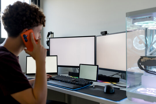 Young man use smartphone at multi-monitor gaming computer