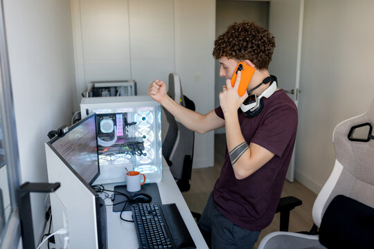 Young man celebrate gaming computer setup with smartphone