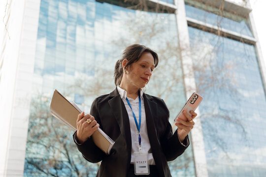 Business Professional Checks Phone While Holding Files Outside Office
