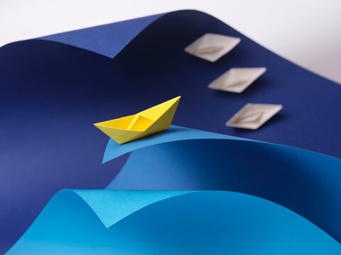 A single yellow paper boat sails on a blue paper wave