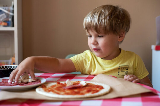Boy putting ingredients on homemade pizza