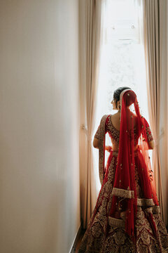 South Asian bride in red lehenga gazing out of a bright window