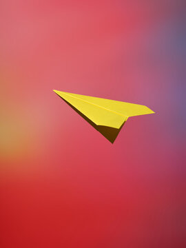 A bright yellow paper airplane soars against a colorful gradient