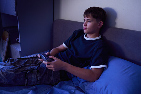 Teen boy gaming late at night in dark bedroom