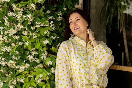 Smiling woman in floral dress beside blooming vine
