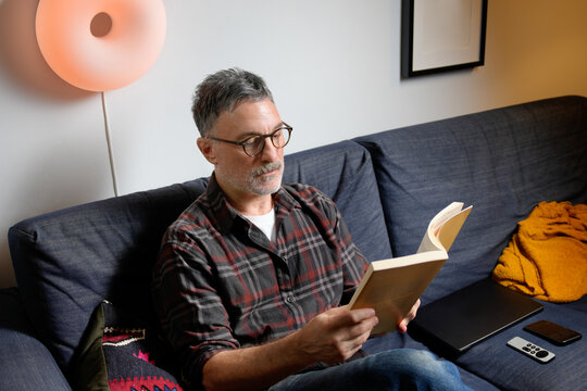 Mature man read book on sofa during remote work break