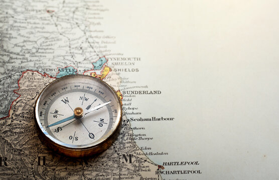 Vintage brass compass on an old England geographic map.  Antique navigation instrument for travel, exploration, geography and discovery concept. Adventure, tourism, cartography and orientation theme.