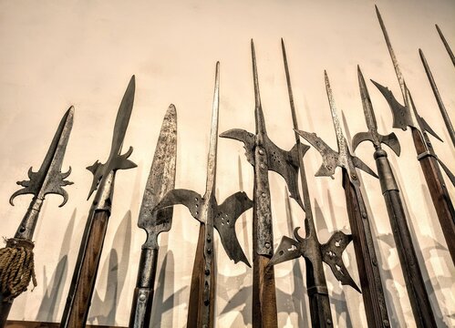 Row of medieval polearms on wall display, low angle close-up view of historical halberds and spears