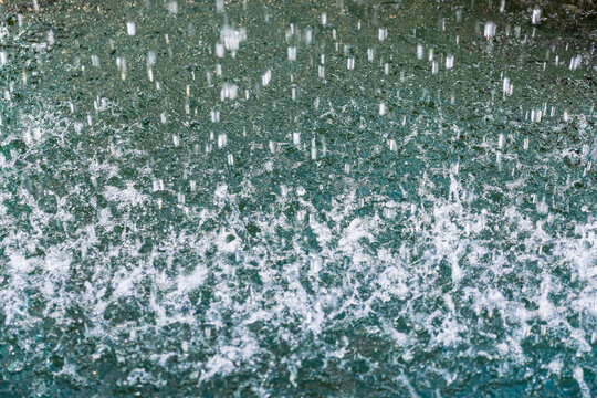Raindrops splash on wet pavement during a heavy shower