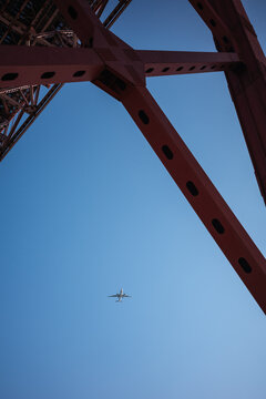 Airplane beneath steel bridge structure against blue sky