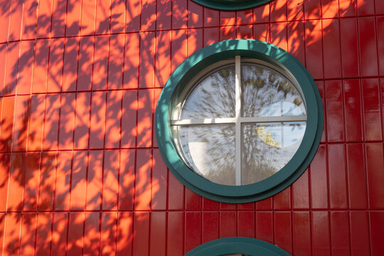 Circular window on red tiled wall with tree shadow