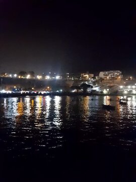 Illuminated coastal bay at night with reflections on calm water and boats