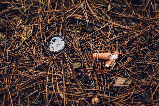 Cigarette butt and bottle cap littering a forest floor