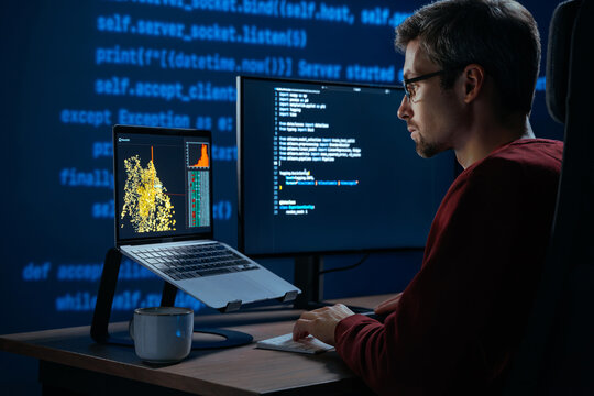 Developer sits in a dimly lit workspace, in front screens displaying code and data science data graph. Focused programmer working, deeply immersed in solving an artificial intelligence problem