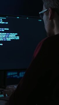 Developer sits in a dimly lit workspace, in front screens displaying data science code. Focused programmer working, deeply immersed in solving an artificial intelligence problem. Vertical video