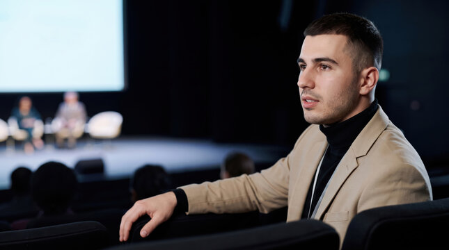 Young businessman attending conference presentation in auditorium