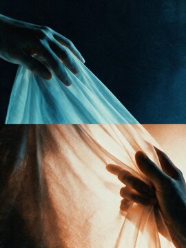 Hands holding translucent fabric in moody dramatic light