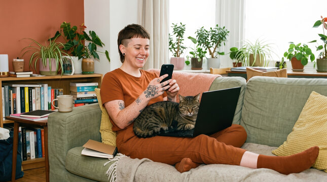 Cat blocks laptop as person checks phone on sofa
