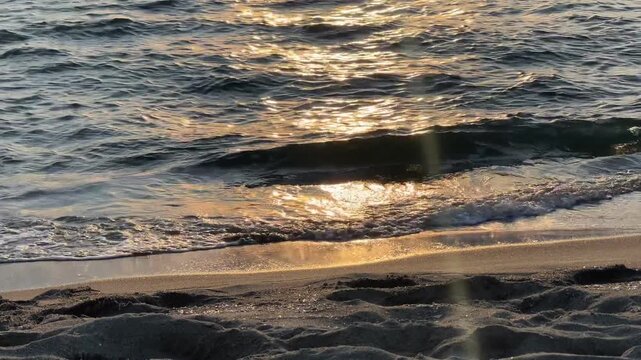 Cinematic golden hour ocean waves splashing on shore, abstract nature background. Serene golden sun reflections on moving sea waters at sunset copy space.
